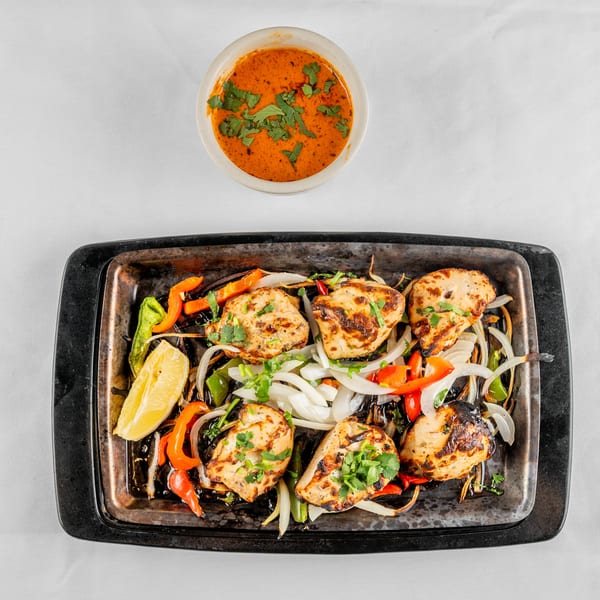 Grilled chicken pieces with bell peppers, onions, and a lemon wedge, served with a side sauce.