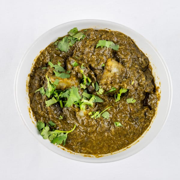 Overhead view of a white bowl filled with a dark green curry, garnished with fresh cilantro.
