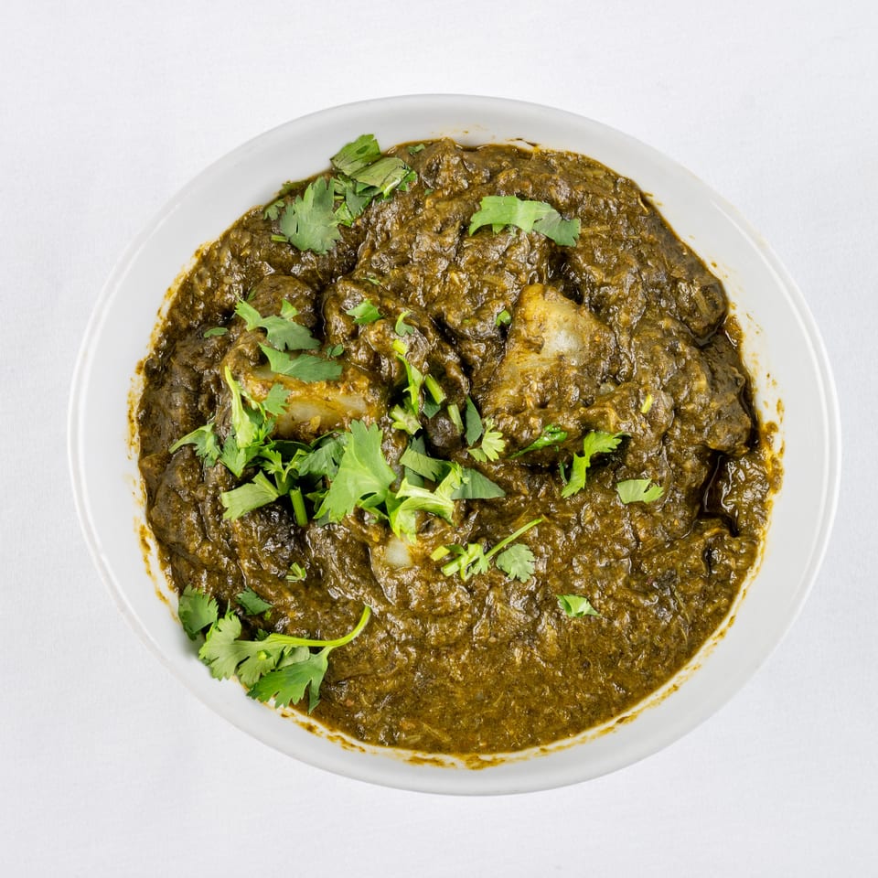 Overhead view of a white bowl filled with a dark green curry, garnished with fresh cilantro.