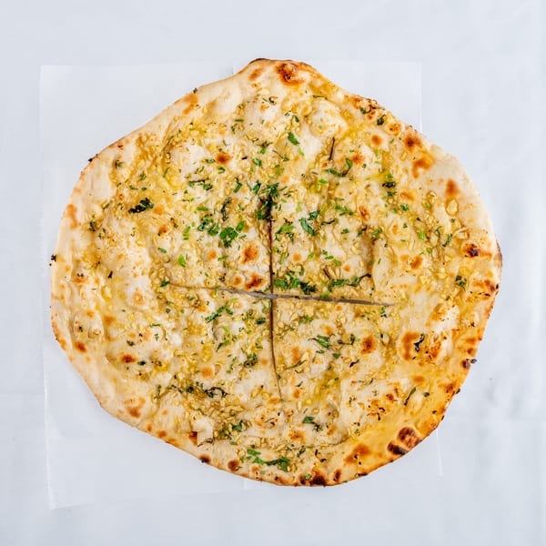 Golden-brown garlic naan bread, topped with minced garlic and fresh green herbs, sliced into four pieces.