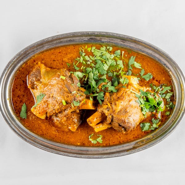 Close-up of tender meat pieces in rich red curry sauce, garnished with fresh cilantro in an oval serving dish.