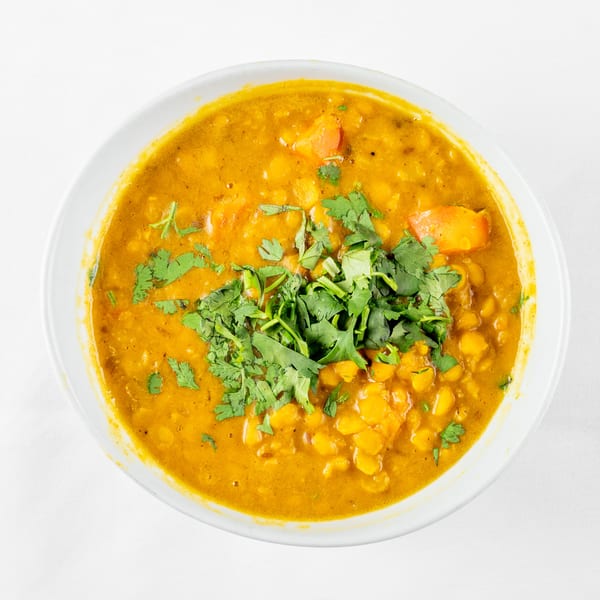Overhead view of a bowl of yellow lentil soup with carrots and fresh cilantro on a white tablecloth.
