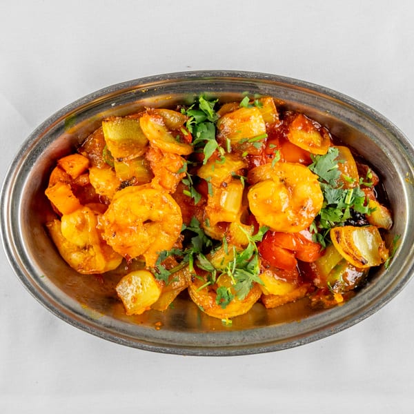 Shrimp and vegetables in a rich orange sauce, garnished with cilantro, served in a metal dish.
