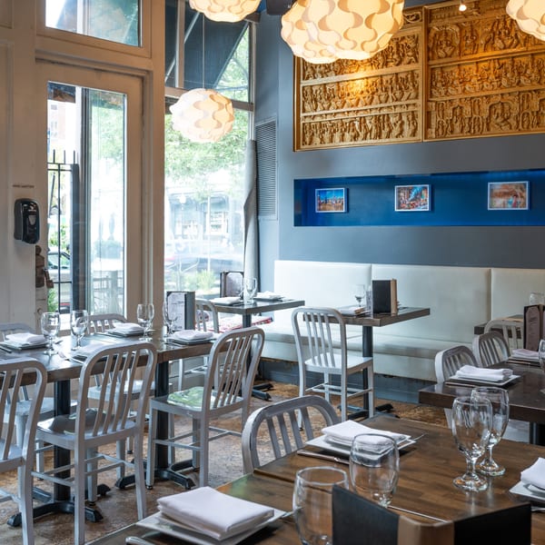 Empty restaurant interior with set tables, white chairs, and decorative wall carvings under unique light fixtures.