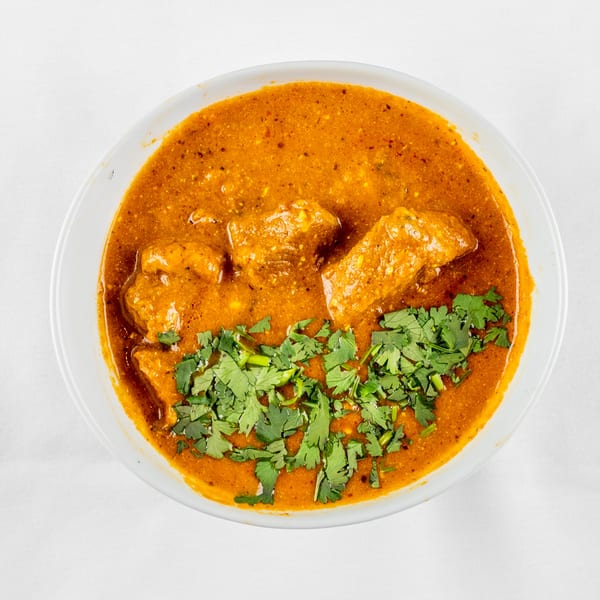 Overhead view of a bowl of orange curry with chicken pieces and fresh green cilantro garnish.