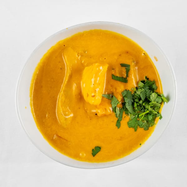 Overhead view of a bowl of orange curry with paneer and fresh cilantro on a white tablecloth.