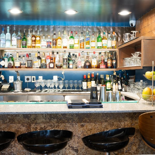 A well-stocked bar with various liquor bottles, glassware, and bar stools in a restaurant setting.