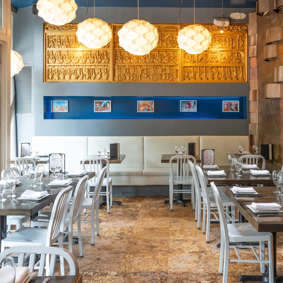An empty restaurant dining room with set tables, white chairs, and decorative wall art.