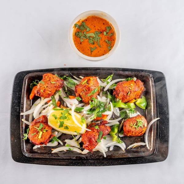 Sizzling chicken tikka with onions, peppers, lemon, and cilantro, served with a side of sauce.